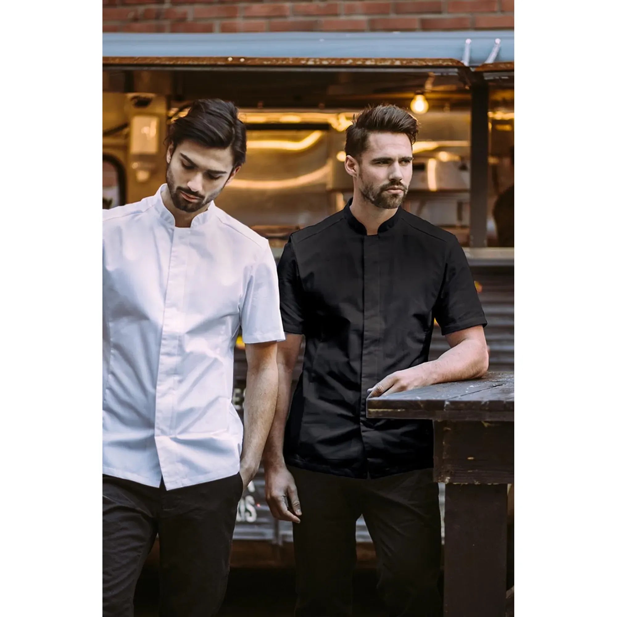 Two men in chef uniforms standing in a kitchen setting.