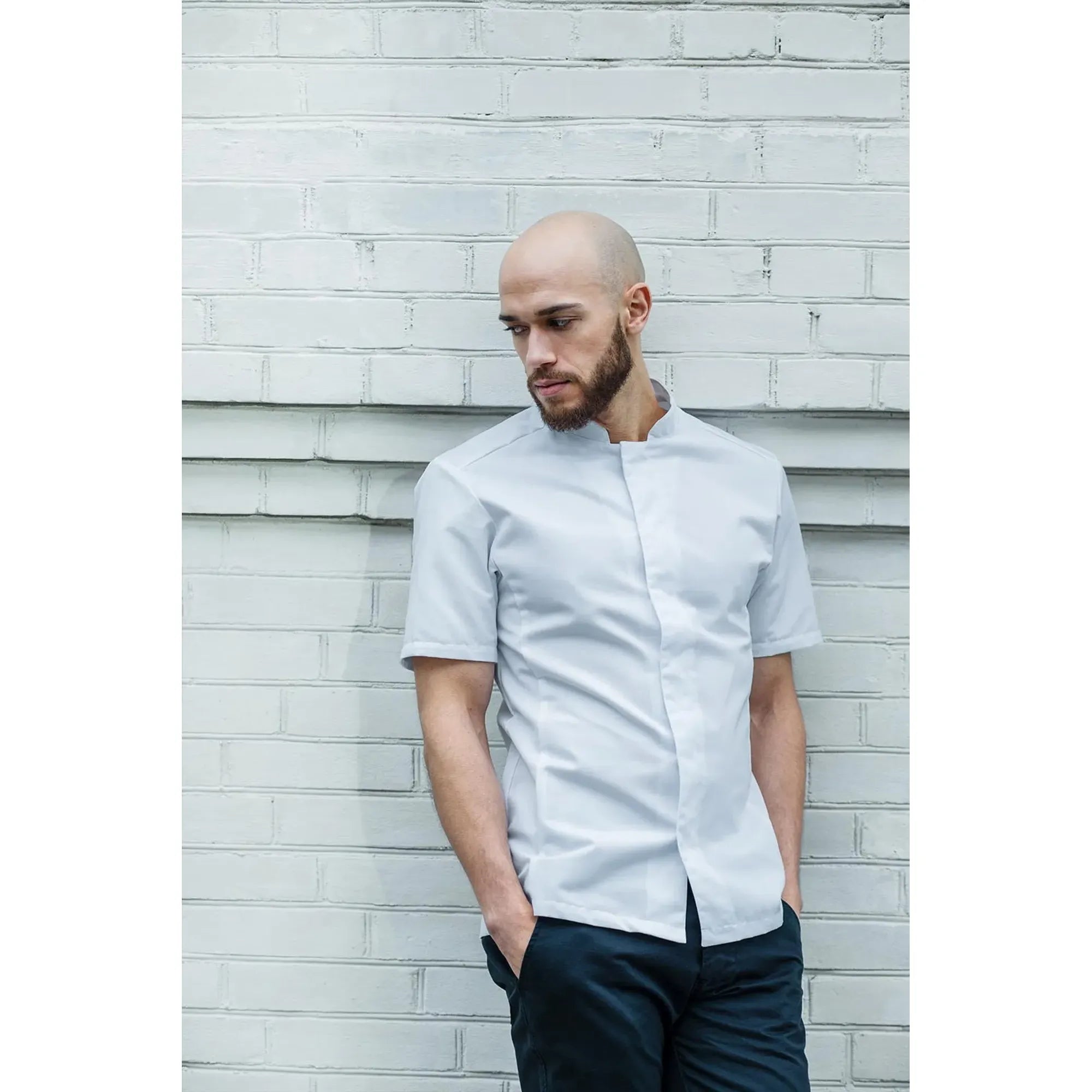 Man wearing a white short-sleeve shirt against a light brick wall.
