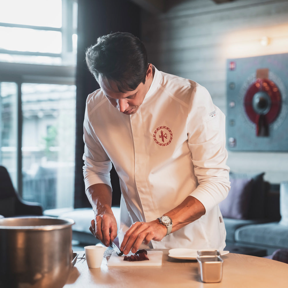 A private chef wearing a long-sleeve white French chef coat with breathable side vents, and custom embroidery.