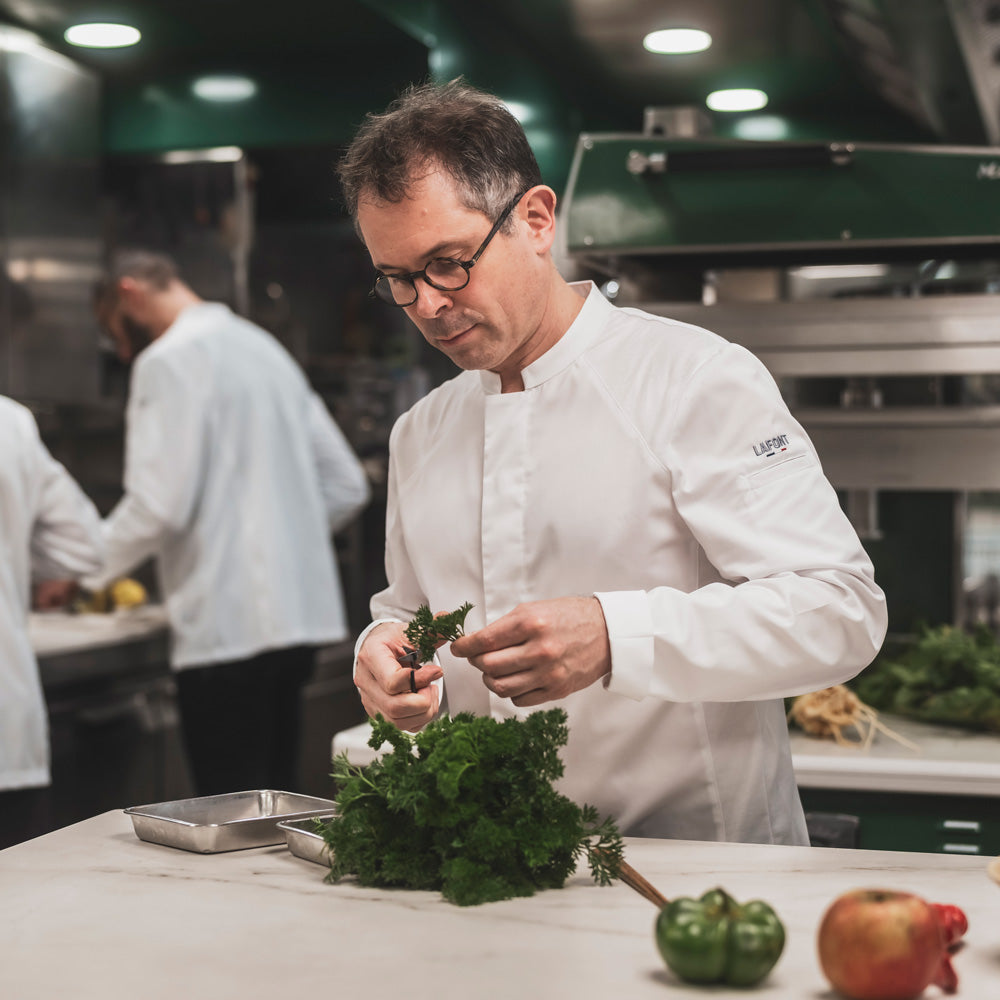 A kitchen chef wearing a long-sleeve white French chef coat with breathable side vents, and hidden snaps, designed for men.