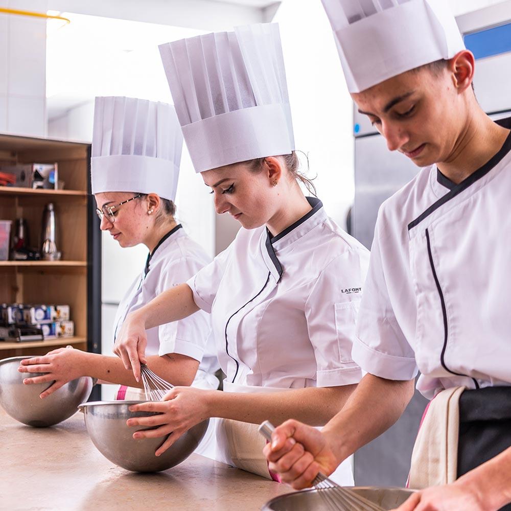 Lafont PARSLEY white with black contrast fabric, short sleeve men's chef coat, 1/4 view seen on a team mixing ingredients in a culinary school.