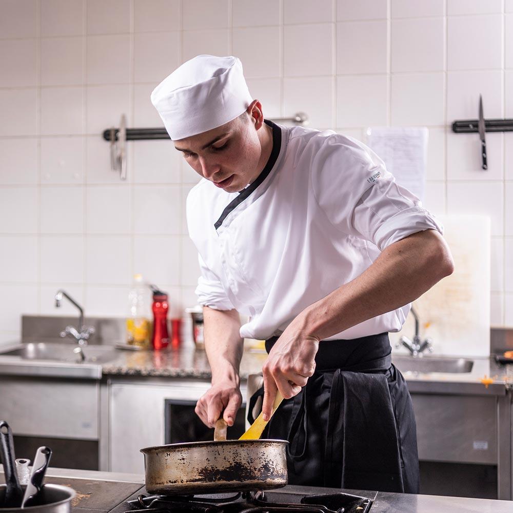 cook in the kitchen wearing a chef coat with the sleeves pushed up.