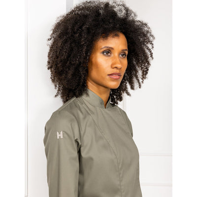 Woman wearing a green chef's jacket with a Le Nouveau Chef brand logo on a white background