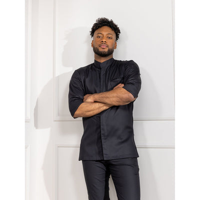 Man wearing a black 3/4-sleeve chef's coat standing against a white wall