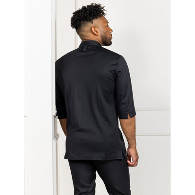 Back side view of a man wearing a black chef's coat standing against a white wall