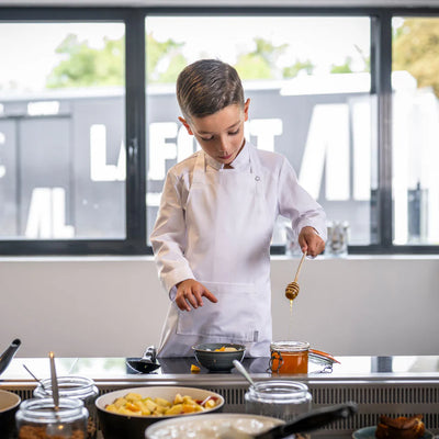 Child in a Lafont chef's apron and jacket preparing food in a kitchen